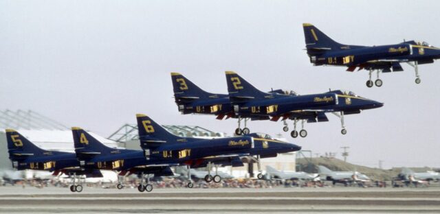 Sześć samolotów A-4 Skyhawk zespołu Blue Angels w ciasnej formacji, widziane z boku na małej wysokości, tuż po oderwaniu się od ziemi